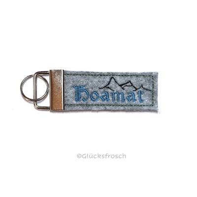 Schlüsselanhänger "Hoamat" aus grauem Filz, gestickt mit Berge im Hintergrund